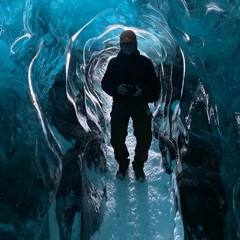 A figure silhouetted in a blue ice tunnel