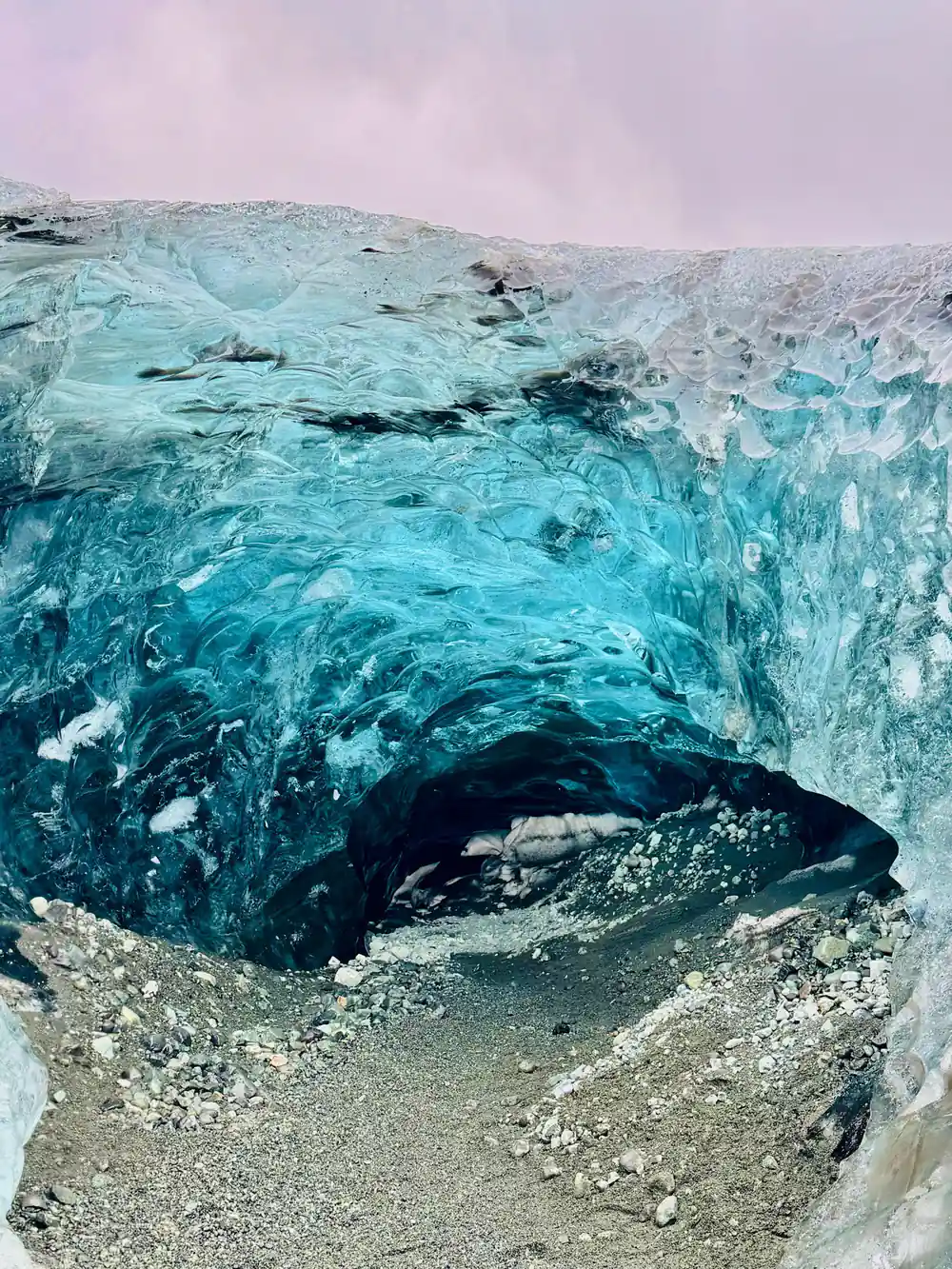 Blue-green glacier cave entrance with snow