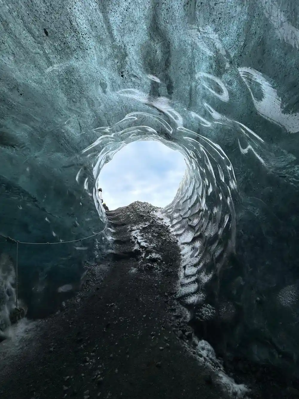 Circular opening in blue glacial ice showing distant landscape