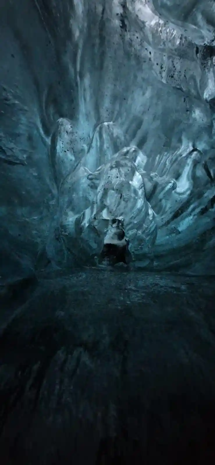 Dark blue-green ice cave interior with person at base