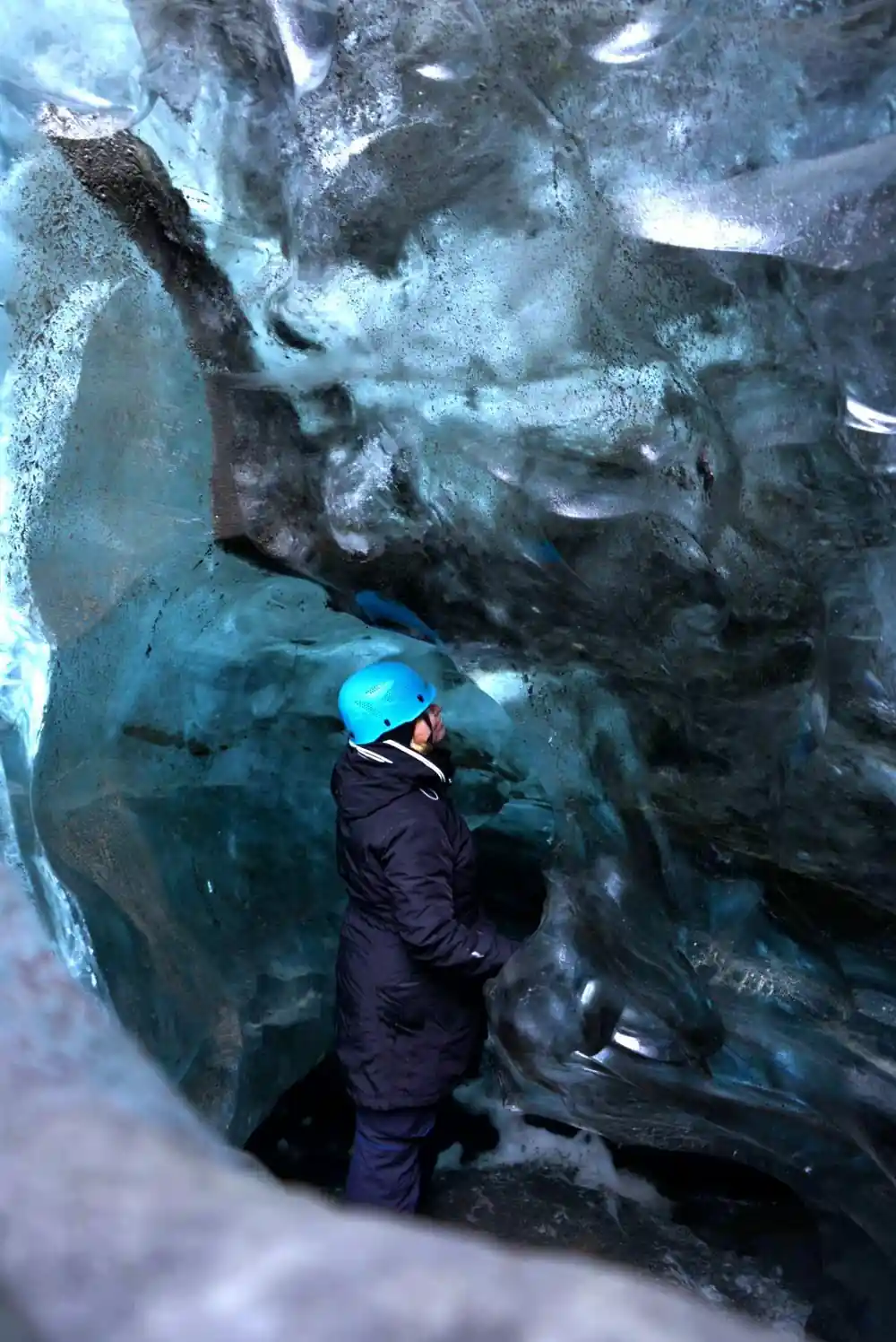 Person climbing inside blue glacier ice cave