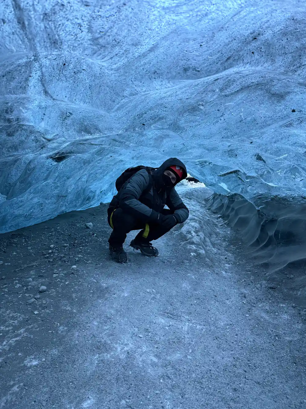Person crouching beneath translucent blue ice overhang