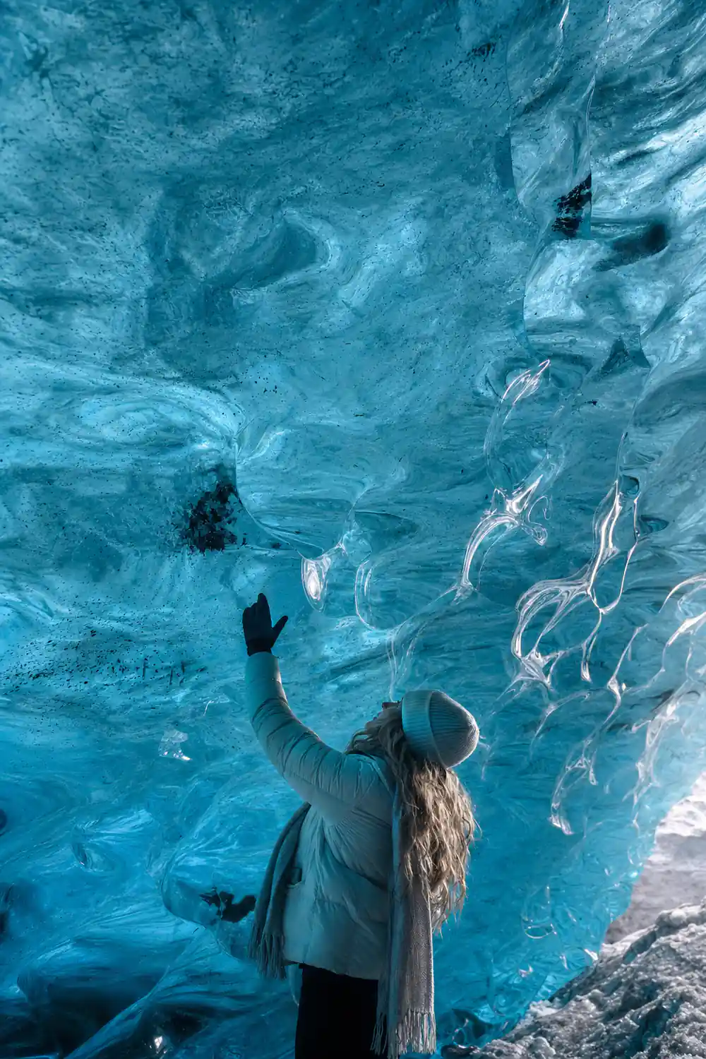 Person inside ice cave looking up at blue glacial ice