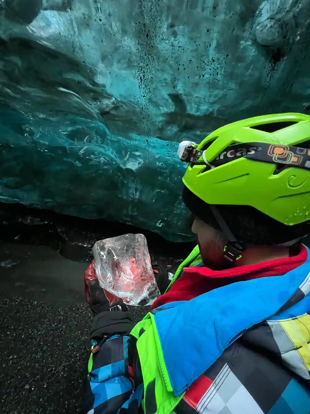 Person in neon gear holding ice chunk inside glacier cave