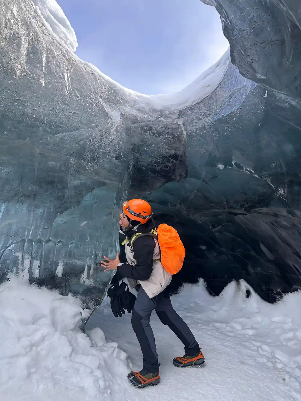Person in orange backpack beneath arched ice cave ceiling