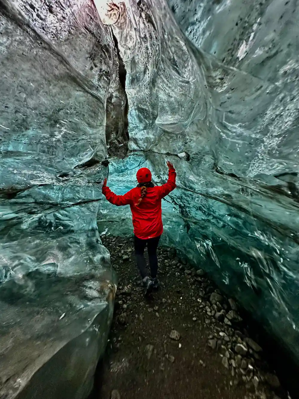 Person in red jacket inside ice cave with arms raised