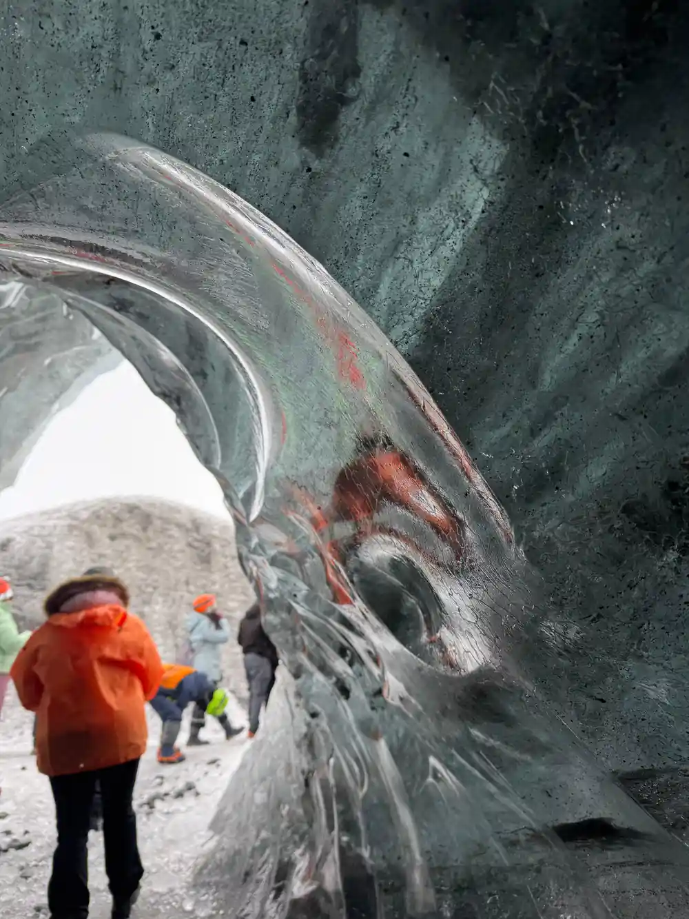 Person in red jacket inside large ice cave opening