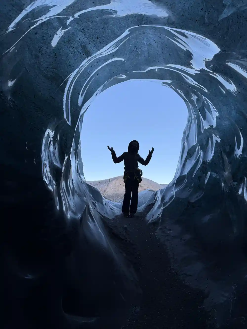 Person silhouetted in circular ice cave tunnel opening