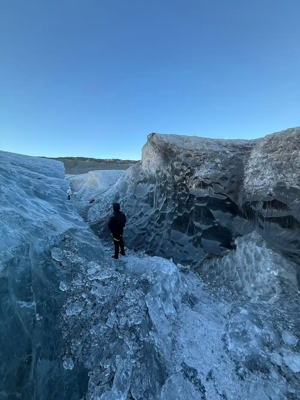 Person standing on rocky ground below towering ice cliff