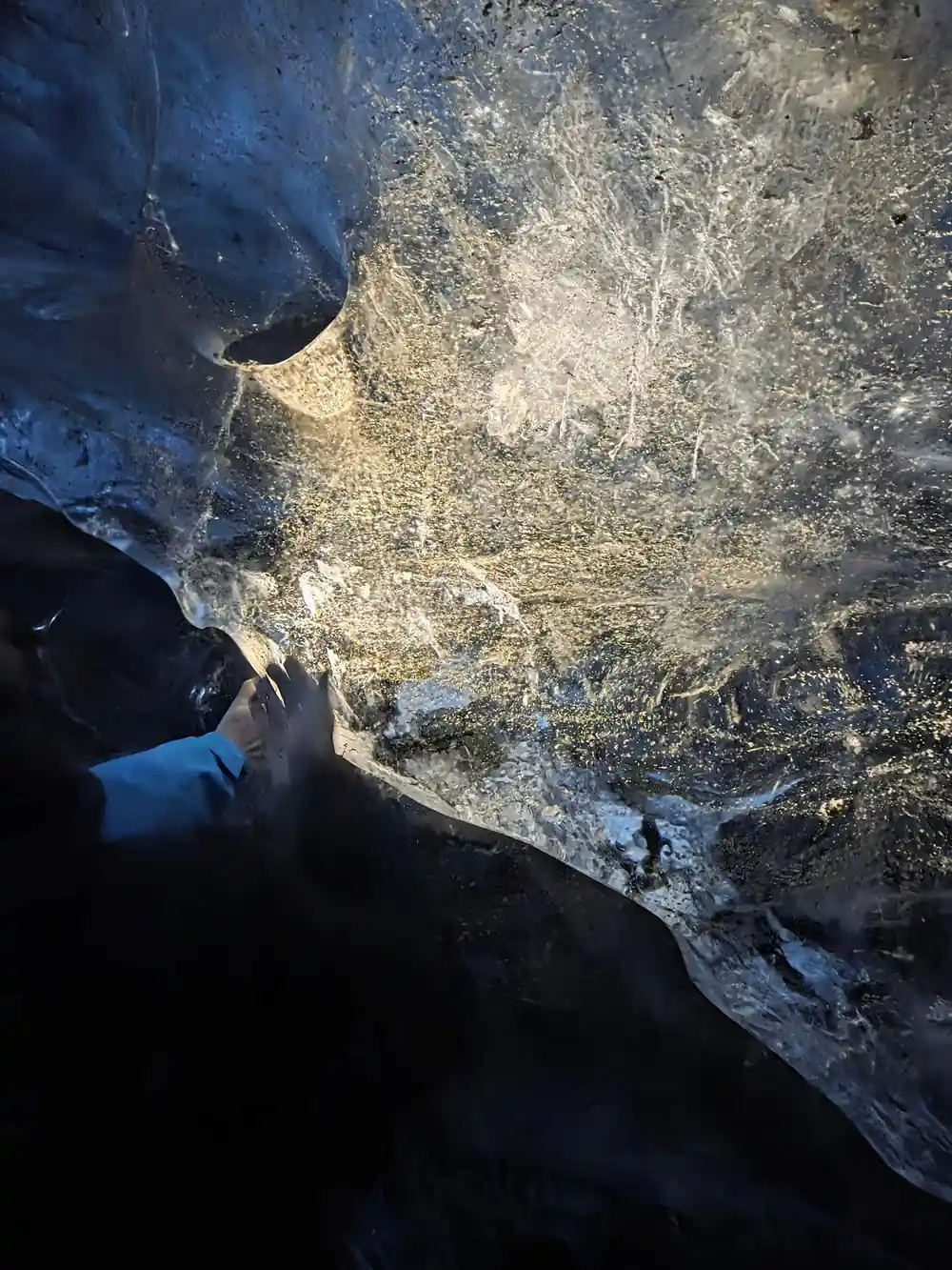 Person touching crystalline ice surface inside glacier cave