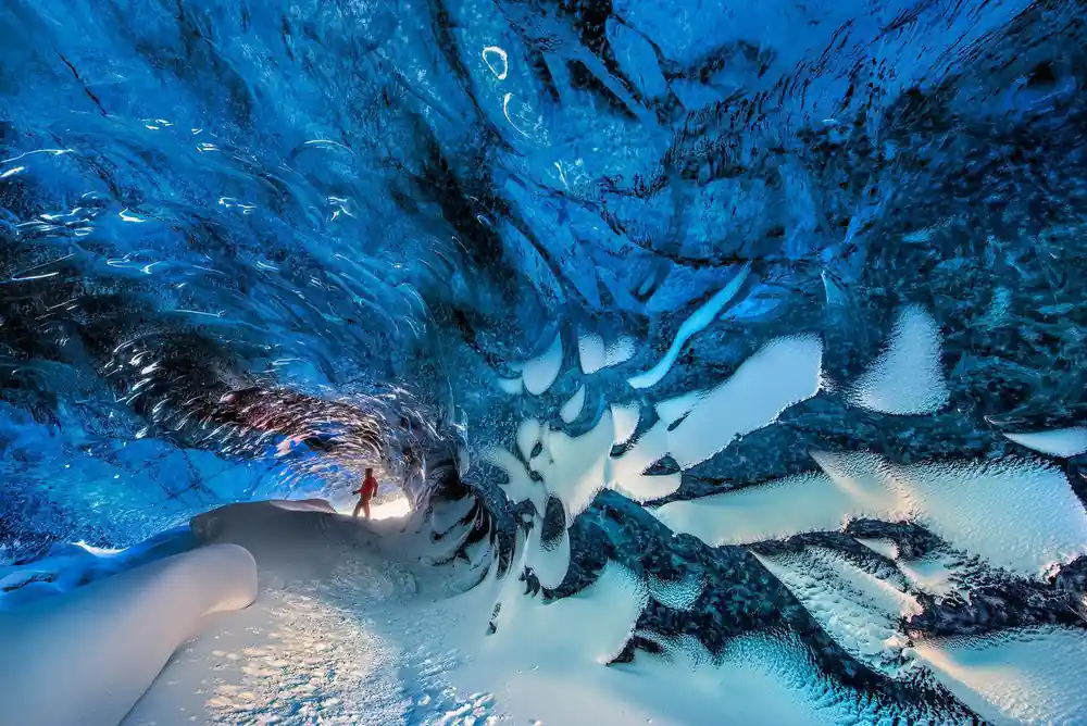Person walking through dramatic blue ice cave formations