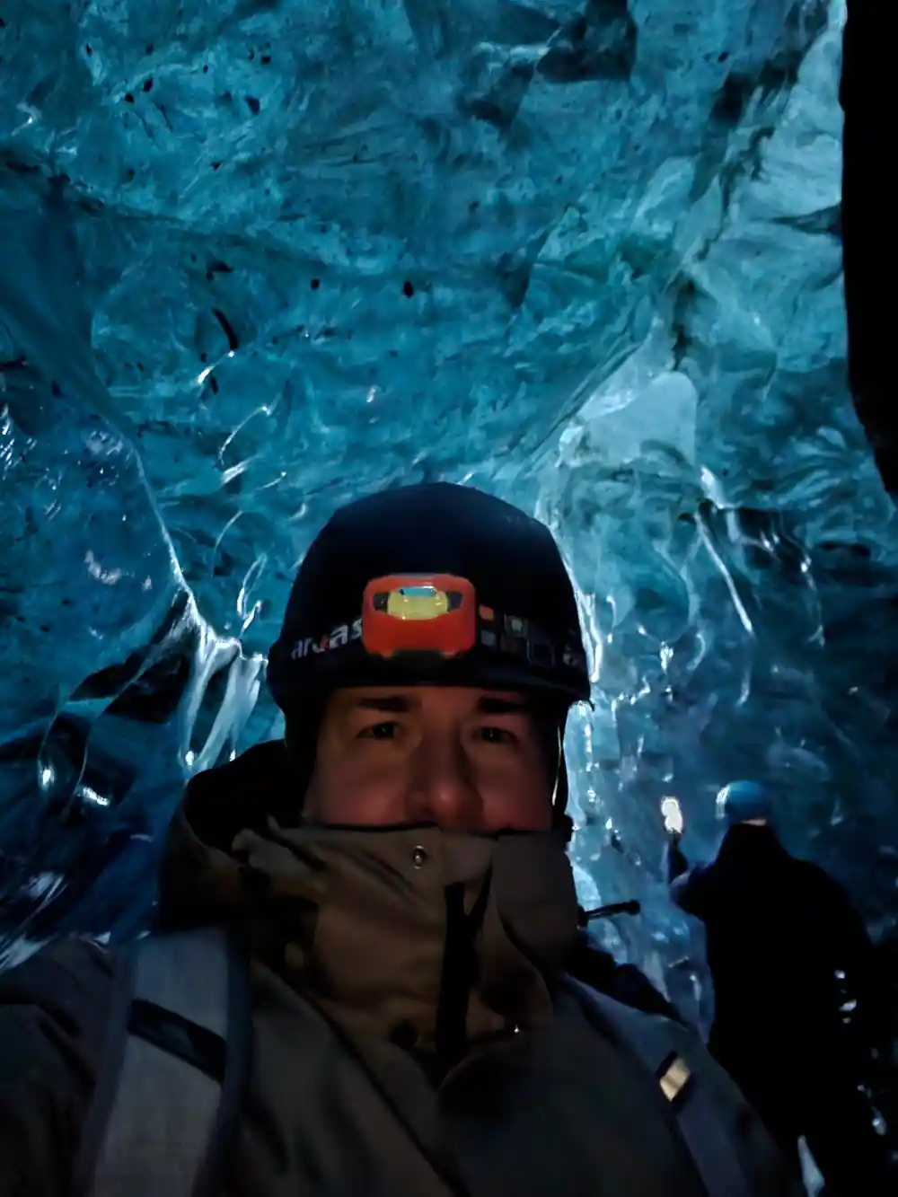 Person wearing headlamp inside bright blue ice cave