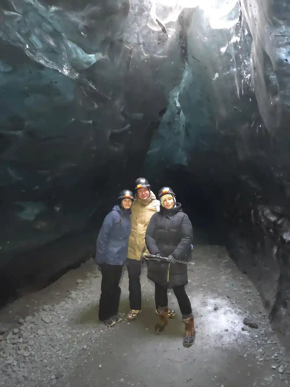 Three people standing inside large ice cave chamber