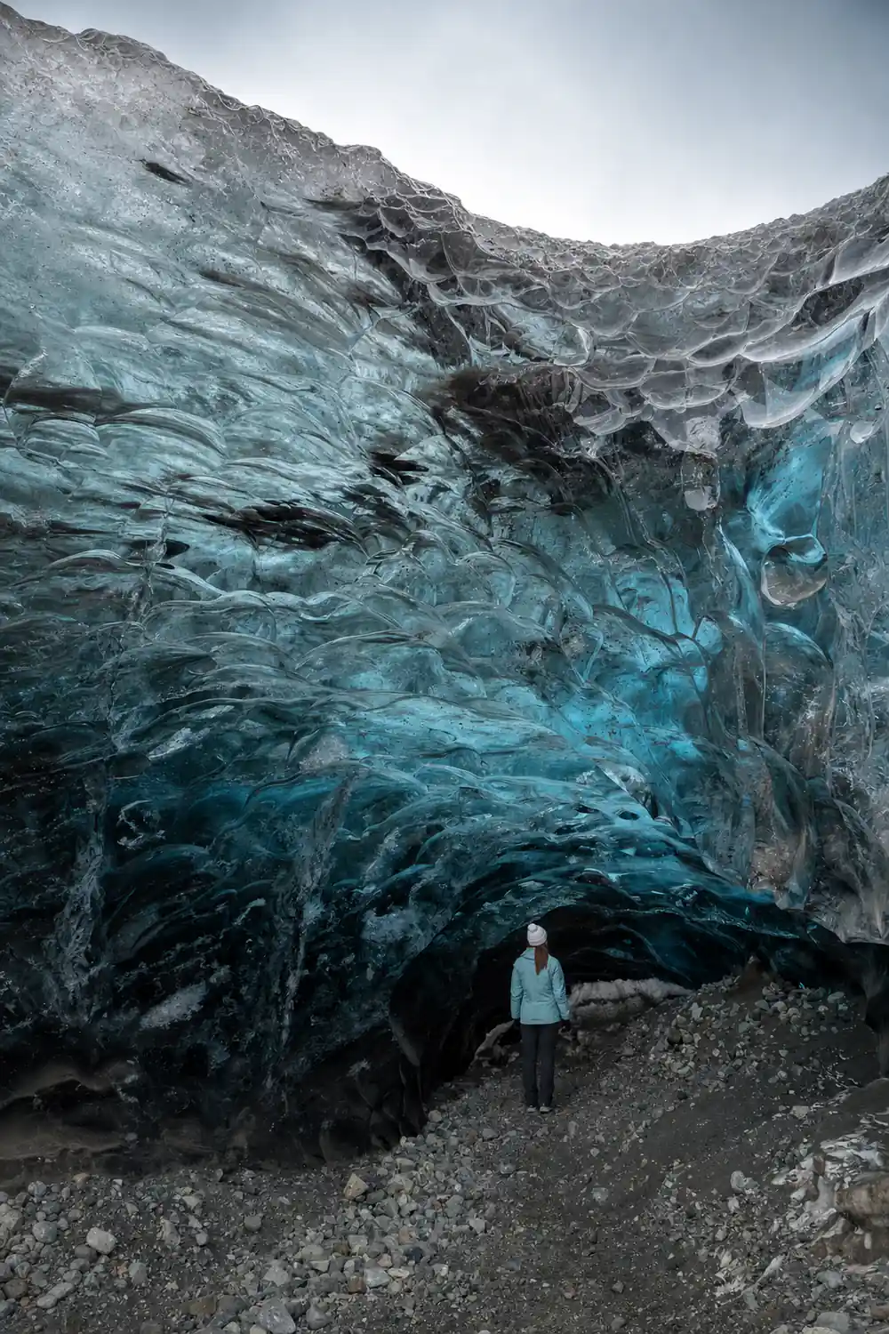 Turquoise glacial ice wall with dark cave entrance below