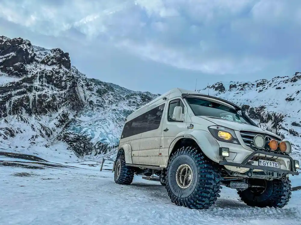 White van with blue wheels on snowy ground, mountains behind