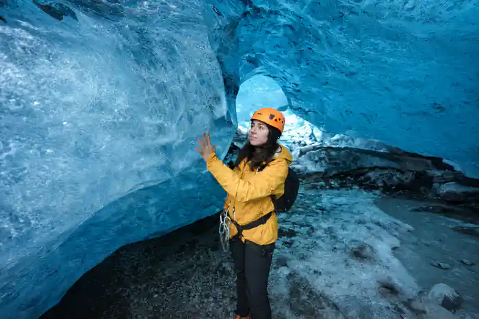 Woman in yellow jacket touching blue ice cave wall